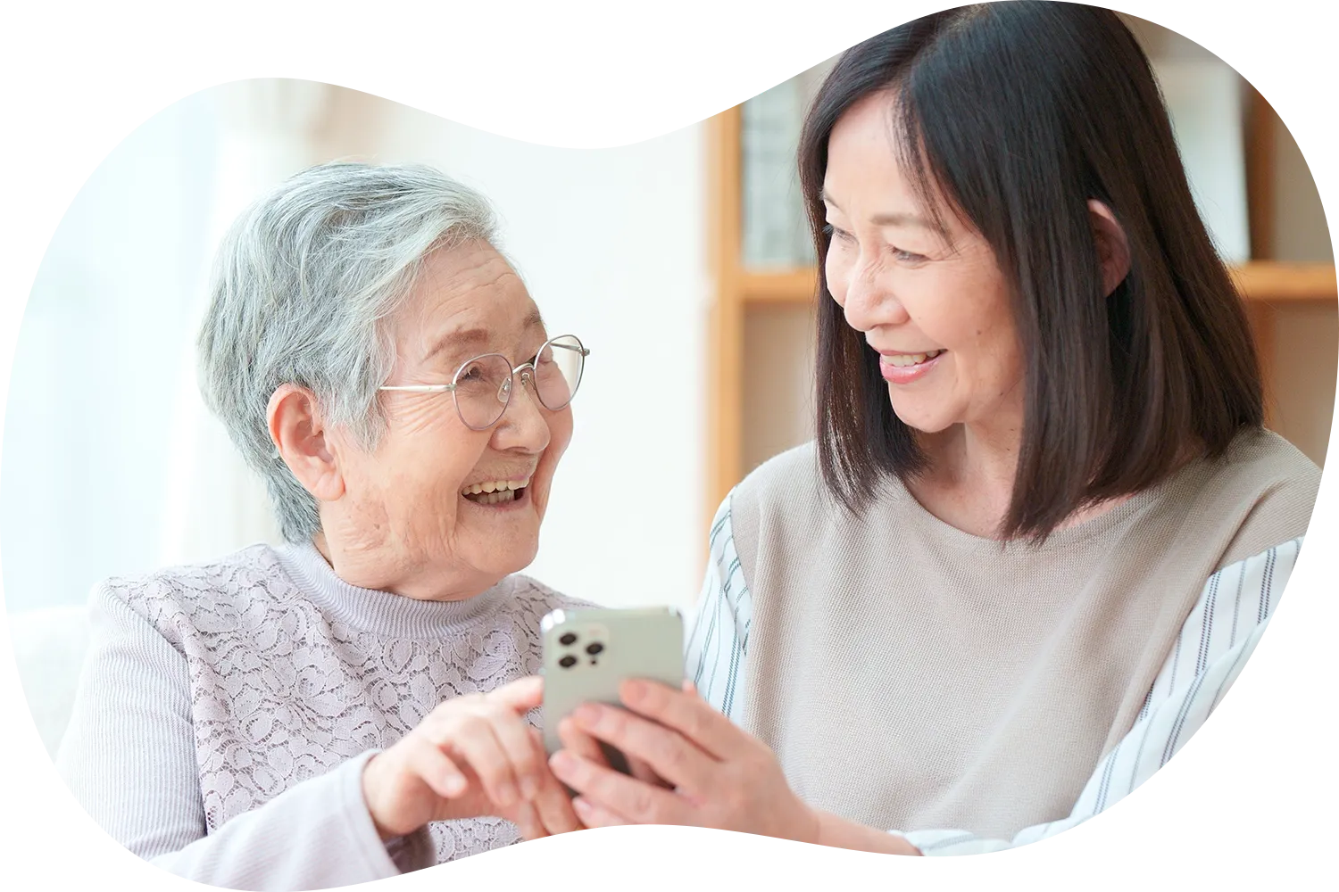 スマートフォンの画面を指さして笑う高齢女性と中年女性の写真